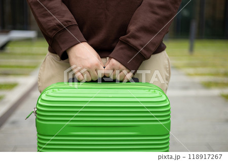 Traveler walking with a suitcase, traveling in the city, cropped view with no face. Passenger waiting at bus station or near hotel. Selective focus on hands holding baggage Traveler walking with a suitcase, traveling in the city, cropped view with no face. Passenger waiting at bus station or near hotel. Selective focus on hands holding baggage 118917267