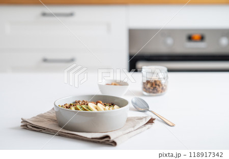 Baked granola with banana and kiwi on the table on a white kitchen background close up. Baked granola with banana and kiwi on the table on a white kitchen background close up. 118917342