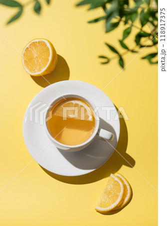 Herbal tea with lemon in a white cup on a yellow background with citrus fruit and slices. 118917375