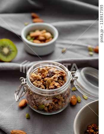 Homemade granola in a jar on a dark linen background with nuts and fruits close up. Homemade granola in a jar on a dark linen background with nuts and fruits close up. 118917395
