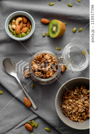 Homemade granola in a jar and bowl on a dark linen background with nuts and fruits. 118917396