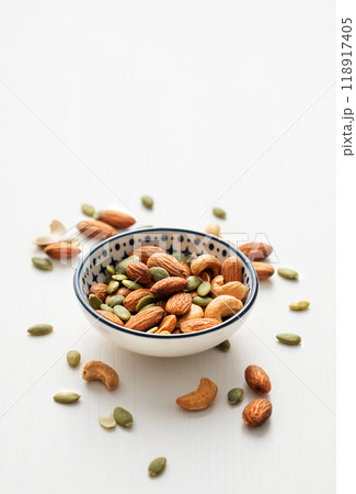 Mix of nuts. Almonds, cashews and pumpkin seeds in a bowl and scattered on a white wooden background Mix of nuts. Almonds, cashews and pumpkin seeds in a bowl and scattered on a white wooden background 118917405