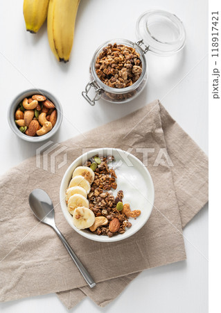 Granola or muesli with yogurt and banana on a white wooden table. Granola or muesli with yogurt and banana on a white wooden table. 118917421