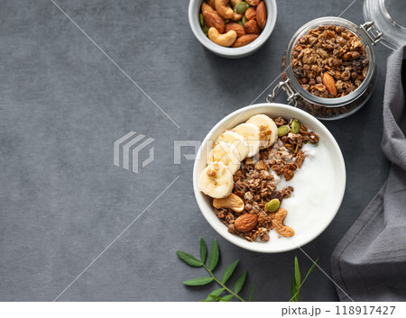 Healthy breakfast. Flat lay of homemade granola or muesli with banana and nuts in a bowl on a dark  background. 118917427