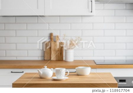 Wooden oak table with a cup of tea and a kettle in front of the kitchen with a white background 118917704