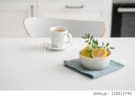 A cup of tea with lemon and a teapot on a white table against the background of a white kitchen. A cup of tea with lemon and a teapot on a white table against the background of a white kitchen. 118917748
