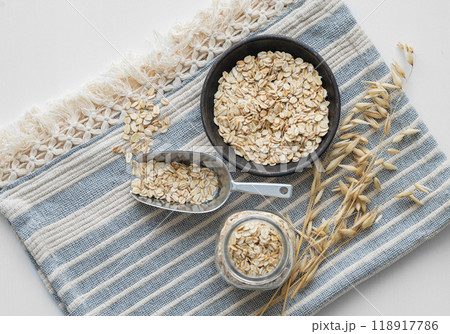 Oatmeal in a plate, jar and in a scoop on a napkin on a white textured background with dry branch. 118917786