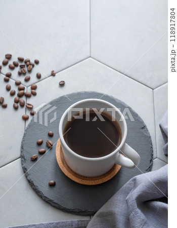 A cup of black coffee on a slate on a trendy gray tile background with coffee beans, napkin  118917804