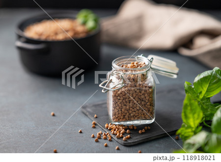 Raw buckwheat grains in a jar on a board on a dark background with fresh herb. Raw buckwheat grains in a jar on a board on a dark background with fresh herb. 118918021