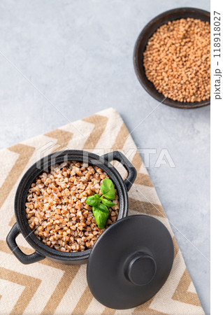 Buckwheat porridge with fresh herbs in a black pan on a light background with dry grain in a bowl. 118918027
