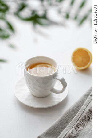 A cup of tea with lemon and green branch on a white table against the background of a kitchen window 118918038