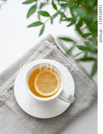 A cup of tea with lemon, napkin and green branch on a white table. 118918041