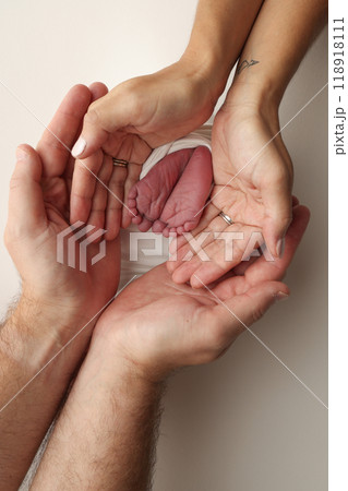 The palms of the parents. A father and mother hold the feet of a newborn child in a white blanket on a white background.. The feet of a newborn in the hands of parents. Photo of foot, heels and toes The palms of the parents. A father and mother hold the feet of a newborn child in a white blanket on a white background.. The feet of a newborn in the hands of parents. Photo of foot, heels and toes 118918111