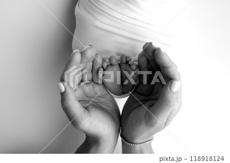 The palms of the parents. A father and mother hold the feet of a newborn child in a blanket. The feet of a newborn in the hands of parents. Black and white Photo of foot, heels and toes The palms of the parents. A father and mother hold the feet of a newborn child in a blanket. The feet of a newborn in the hands of parents. Black and white Photo of foot, heels and toes 118918124