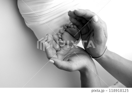 The palms of the parents. A father and mother hold the feet of a newborn child in a blanket. The feet of a newborn in the hands of parents. Black and white Photo of foot, heels and toes The palms of the parents. A father and mother hold the feet of a newborn child in a blanket. The feet of a newborn in the hands of parents. Black and white Photo of foot, heels and toes 118918125