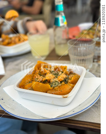 Plate of savory pasta shells with creamy sauce is perfectly presented on a white dish, depicting an inviting and appetizing meal in casual dining setting. the background hints at relaxed social 118920381