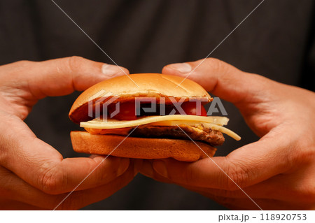 Ready to eat tasty fast food hamburger. Unhealthy food concept. Hands holding homemade beef burger on wooden table. Man holds burger with hands. Home delivery. Close up shot of young man eats burger. 118920753