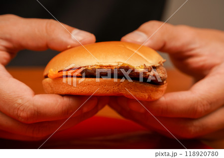 Man holds burger with hands. Hands holding homemade beef burger on wooden table. Ready to eat tasty fast food hamburger. Unhealthy food concept. Home delivery. Close up shot of young man eats burger. 118920780