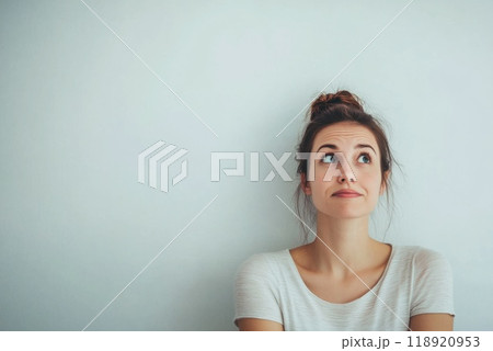 A young woman with a thoughtful expression sitting against a plain wall while contemplating her next decision 118920953
