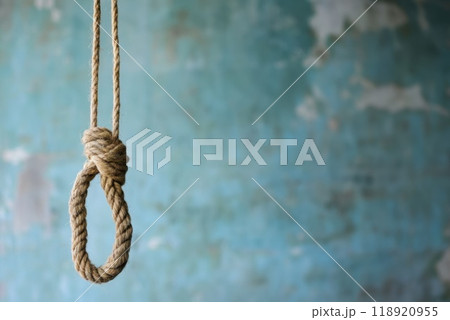 A close up view of a noose made from natural rope hanging against a textured blue wall in dim light A close up view of a noose made from natural rope hanging against a textured blue wall in dim light 118920955