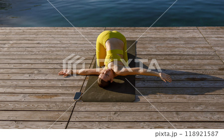 A Woman Practicing Yoga in a Bright Yellow Outfit by the Calm and Serene Water Side 118921587