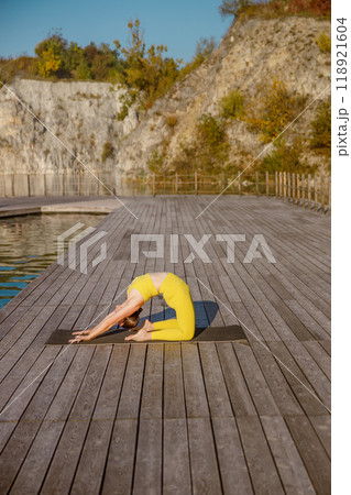 Engaging in a Yoga Pose by the Water during the serene season of Autumn and its beauty Engaging in a Yoga Pose by the Water during the serene season of Autumn and its beauty 118921604