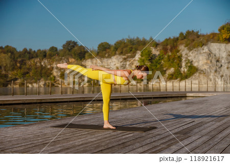 Engaging in a Yoga Pose at Sunrise on a Beautiful and Scenic Waterfront Location 118921617