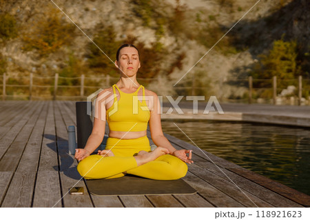 Enjoying a Peaceful Yoga Practice by the Lovely Lake While Dressed in Vibrant Yellow Attire Enjoying a Peaceful Yoga Practice by the Lovely Lake While Dressed in Vibrant Yellow Attire 118921623