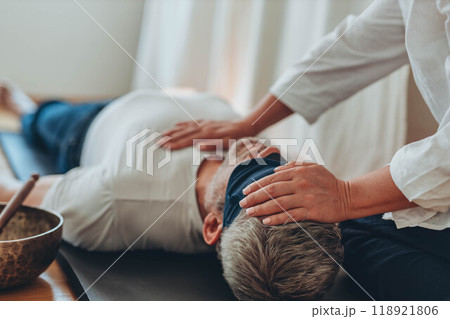 A man lying on a mat with a blindfold, practicing breathing exercises while a woman acts as a coach, assisting him 118921806