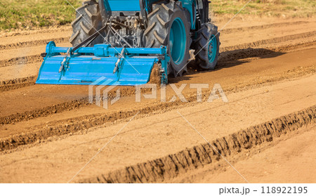 Tractor cultivating land with a rotary tiller in farm. 118922195