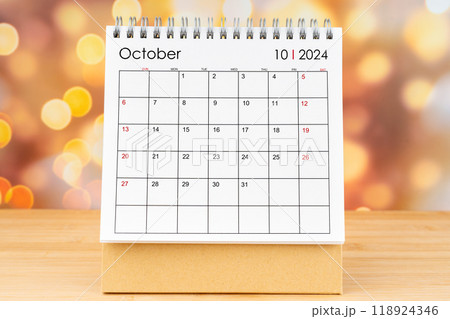October 2024 desk calendar on wooden table with gold light bokeh background. 118924346