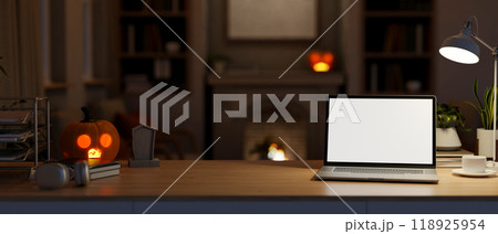 A laptop mockup on a table in a living room on Halloween night, illuminated by glowing lights. 118925954
