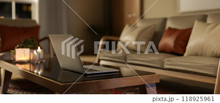 A laptop and candle lights on a dark coffee table in a cozy contemporary living room at night. 118925961