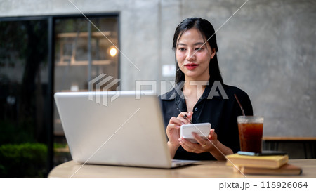 An attractive Asian businesswoman is working remotely from a coffee shop, focused on her work. An attractive Asian businesswoman is working remotely from a coffee shop, focused on her work. 118926064