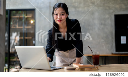An attractive, confident Asian businesswoman is smiling at the camera while leaning on her desk. An attractive, confident Asian businesswoman is smiling at the camera while leaning on her desk. 118926092
