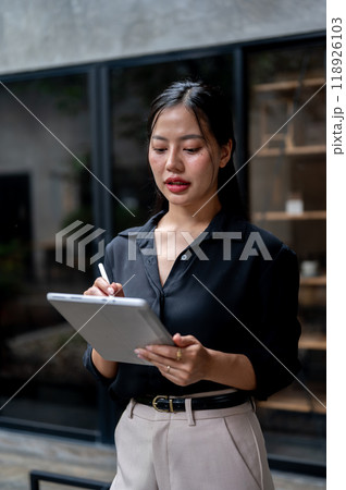 Professional Asian businesswoman is focused on reading her work on her digital tablet in her office. 118926103