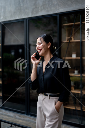 A confident Asian businesswoman is having a conversation on the phone while standing in her office. 118926104