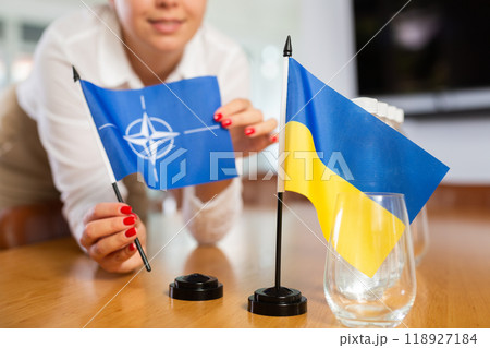 Unrecognizable girl sets midget flags of Ukraine and NATO before international negotiations 118927184