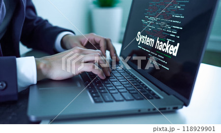 Close-up view of hands typing on laptop with screen showing cyber attack message, red and white text alerting system hack, concept of data protection failure, cybersecurity threat illustration 118929901