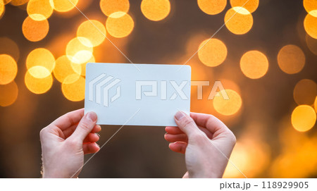 Close-up hand holding mockup white card ready for branding, against backdrop of soft glowing bokeh lights, business or personal graphic design Close-up hand holding mockup white card ready for branding, against backdrop of soft glowing bokeh lights, business or personal graphic design 118929905