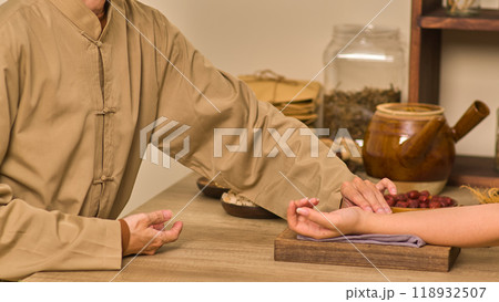 A practitioner of traditional medicine checks a patient's veins by placing the patient's hand on a towel-covered wooden board, with required supplies and medication packets arranged around the table. A practitioner of traditional medicine checks a patient's veins by placing the patient's hand on a towel-covered wooden board, with required supplies and medication packets arranged around the table. 118932507
