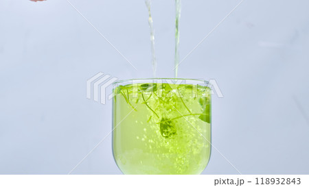 Spherical flask containing green solution with gotu kola samples being poured from above by a scientist, sample image in a laboratory with white walls. 118932843