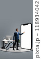 Businessman with suitcase pointing to large 3D model of phone with blank screen, representing seamless business travel and mobile convenience for professionals on the go. 118934042