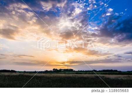 Golden sunrise or sunset in the cloudy sky with sun rays in summer over the meadow 118935683
