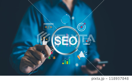 SEO Search Engine Optimization Concept. Businessman hold magnifying glass focuses highlighting SEO, surrounded by various digital marketing icons, representing search engine optimization strategies. 118937848