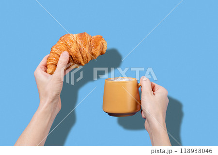 Women's hands hold fresh croissant and cup of coffee  on a blue background.  118938046