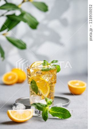 Iced tea with lemon, mint and ice in a glass on a light background with shadow and branch. Iced tea with lemon, mint and ice in a glass on a light background with shadow and branch. 118938052