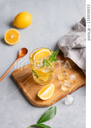 Iced drink with lemon, mint in a glass on a wooden board on a light background with citrus fruits. Iced drink with lemon, mint in a glass on a wooden board on a light background with citrus fruits. 118938053