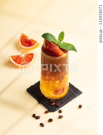 Espresso coffee with orange juice (bumble) in a tall glass with ice and mint on a yellow background 118938071