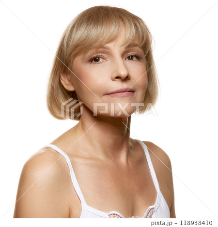 Portrait of middle-aged woman with well-kept skin posing, looking at camera against white studio background. Beauty routine. 118938410